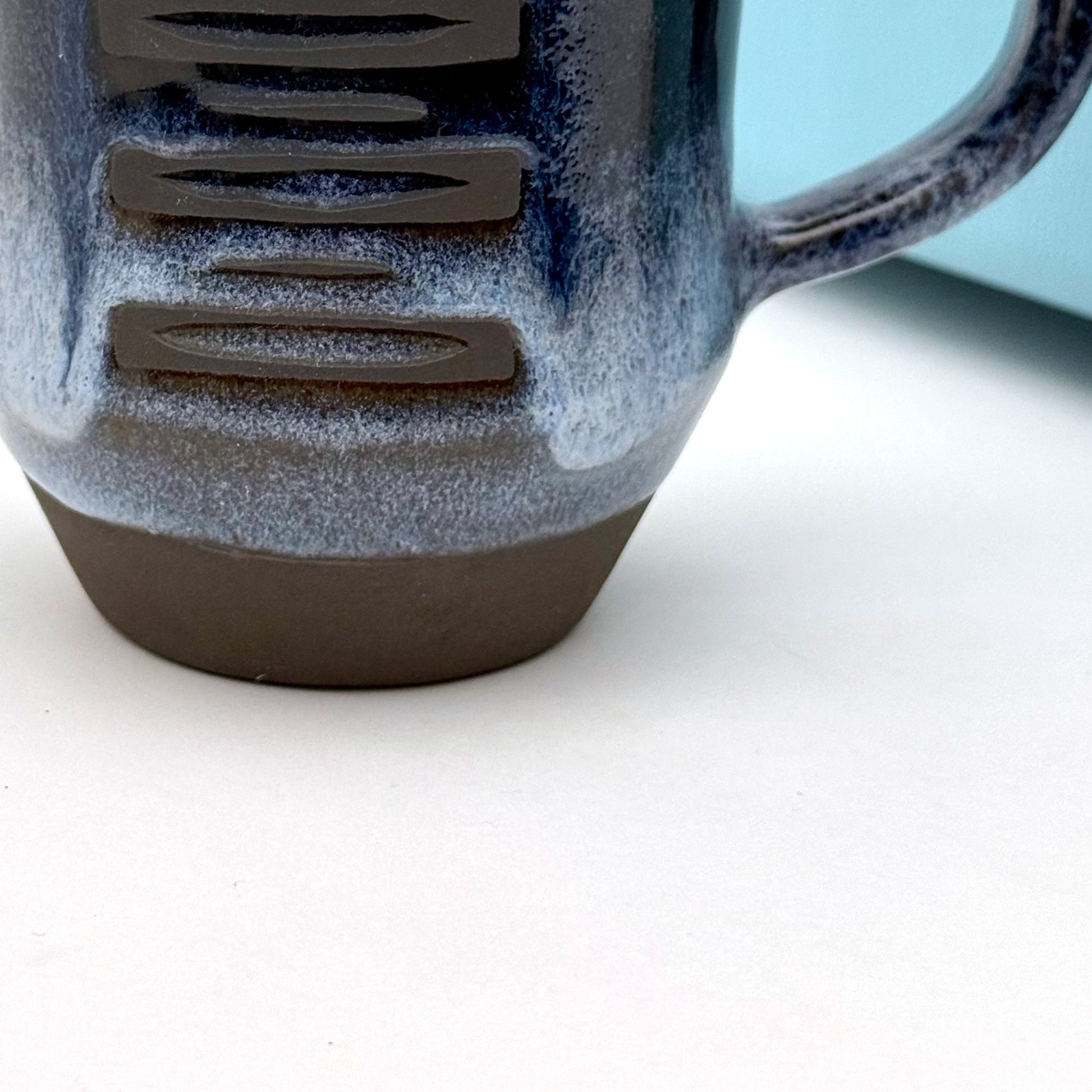 Close-up of handmade ceramic mug with a rounded shape, finished in layered blue glazes and a mid-century–inspired pattern.