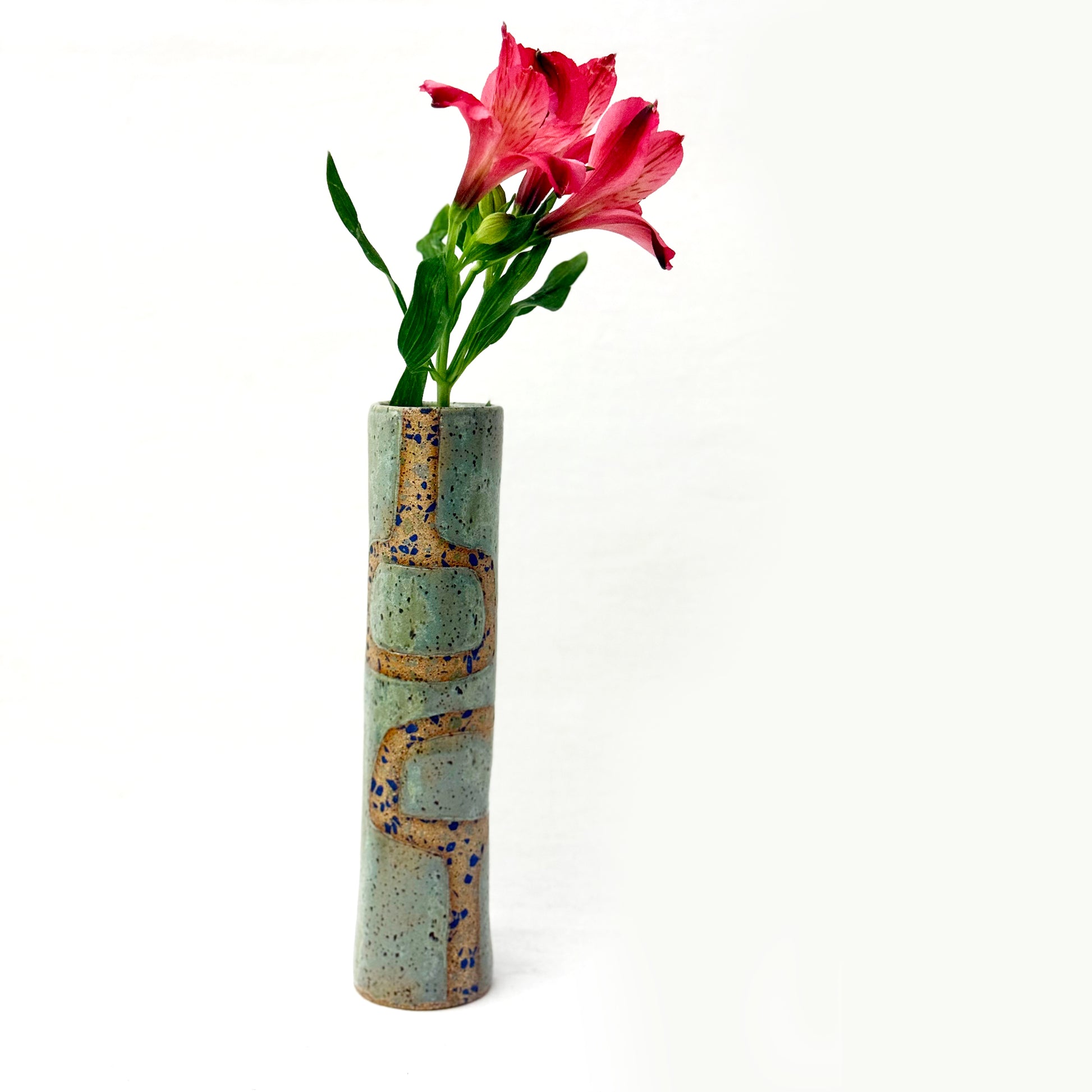 Cylindrical ceramic vase with textured surface holding a pink flower on a white background