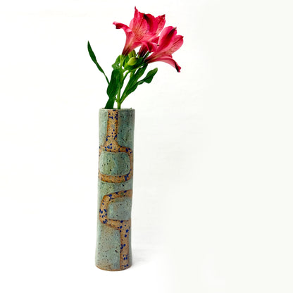 Cylindrical ceramic vase with textured surface holding a pink flower on a white background