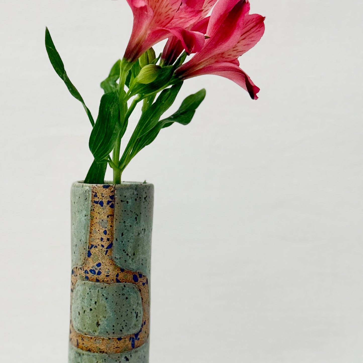 Cylindrical ceramic vase with speckled design containing pink flowers on a light gray background