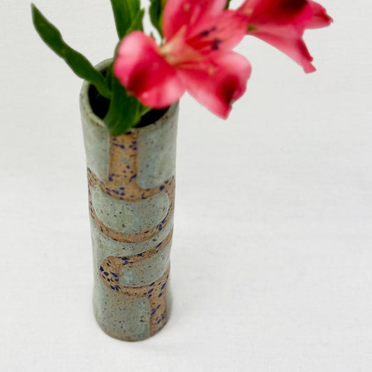 Cylindrical ceramic vase with decorative patterns holding pink flowers on a light background