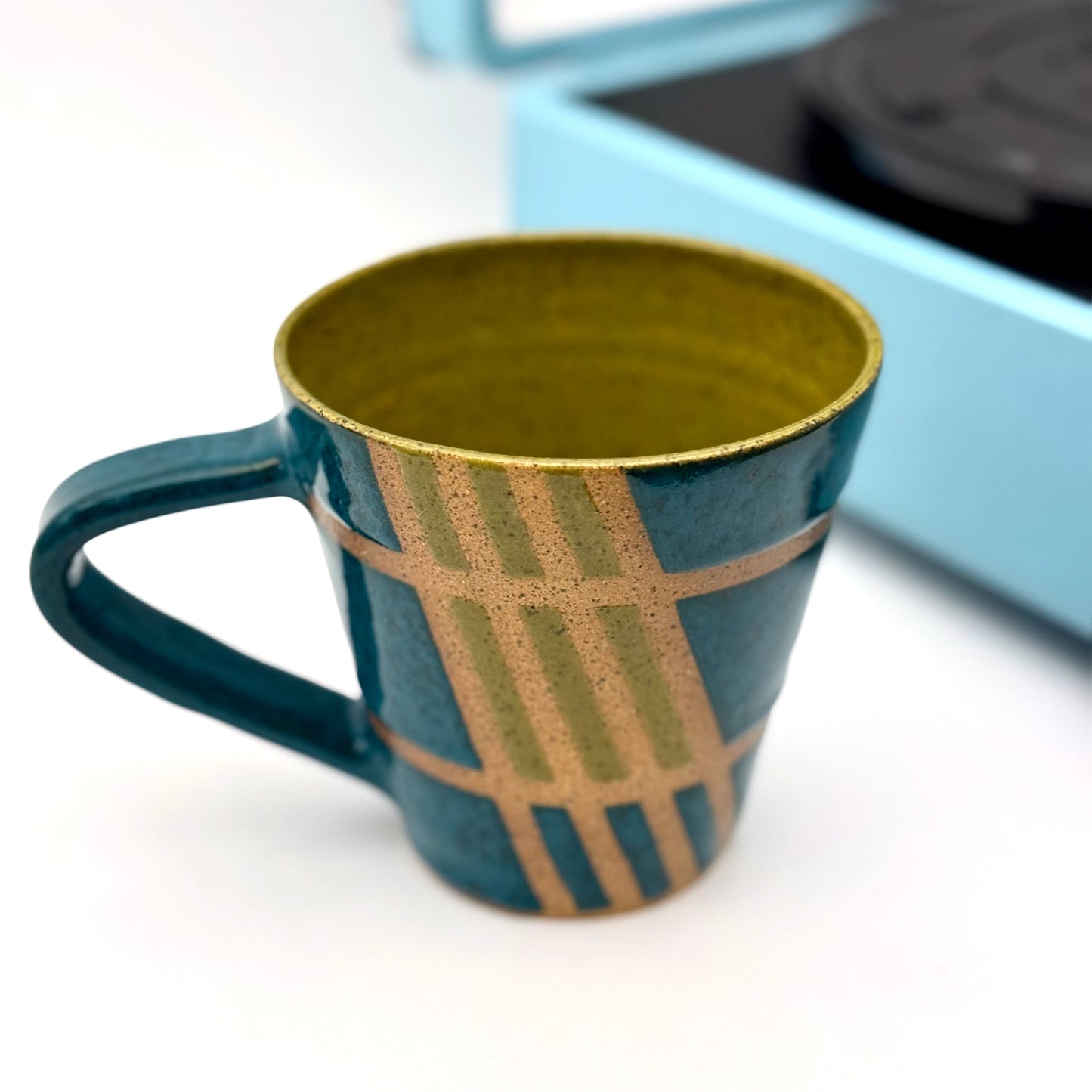 Handmade ceramic mug finished in deep teal and olive glazes with a mid-century–inspired intersecting pattern.