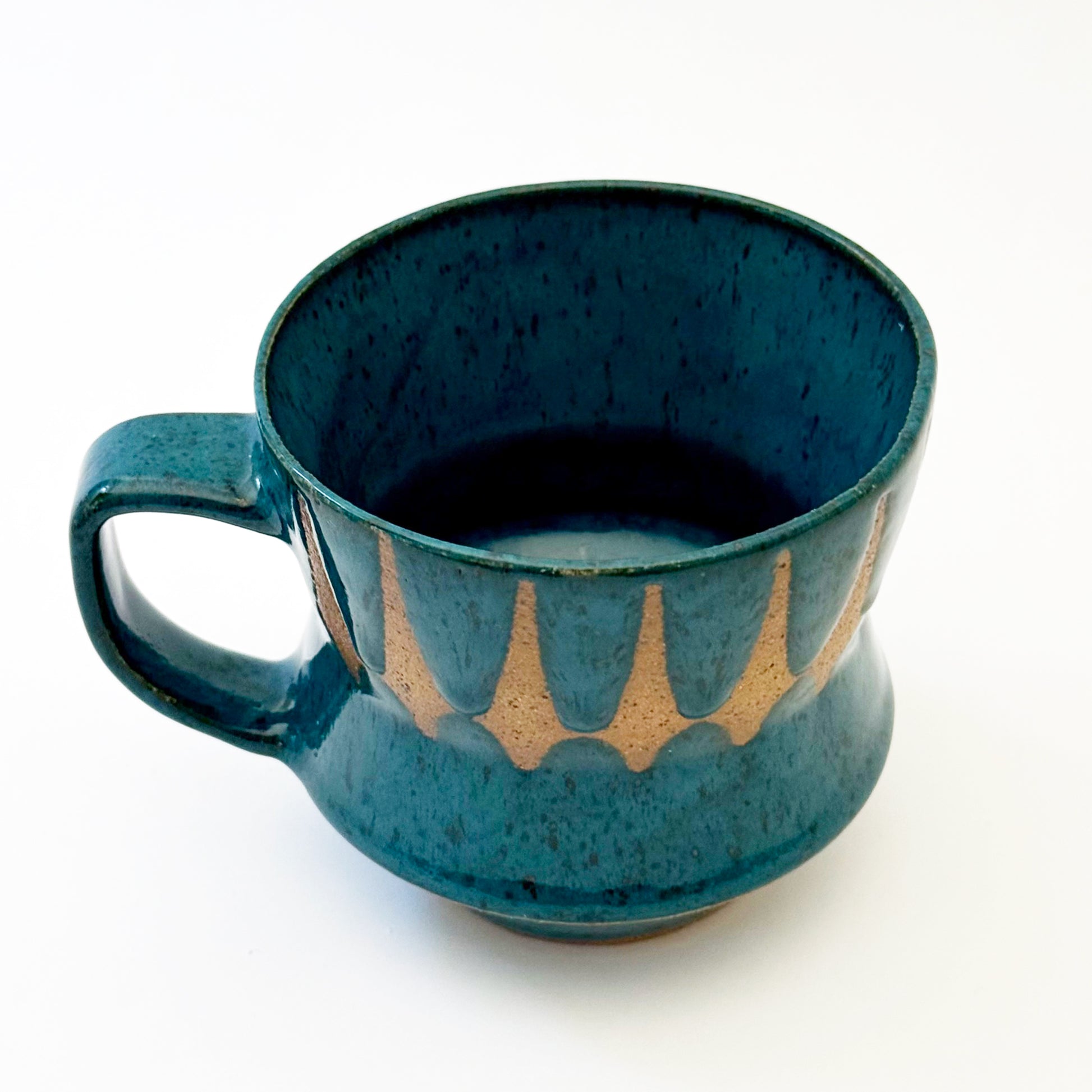 Hand-thrown stoneware mug with layered cobalt and teal blue glaze and a repeating retro geometric pattern in exposed speckled clay. The sculpted mug has a curved waist, angular handle, glossy finish, and mid-century-inspired design. Photographed against a soft white background.