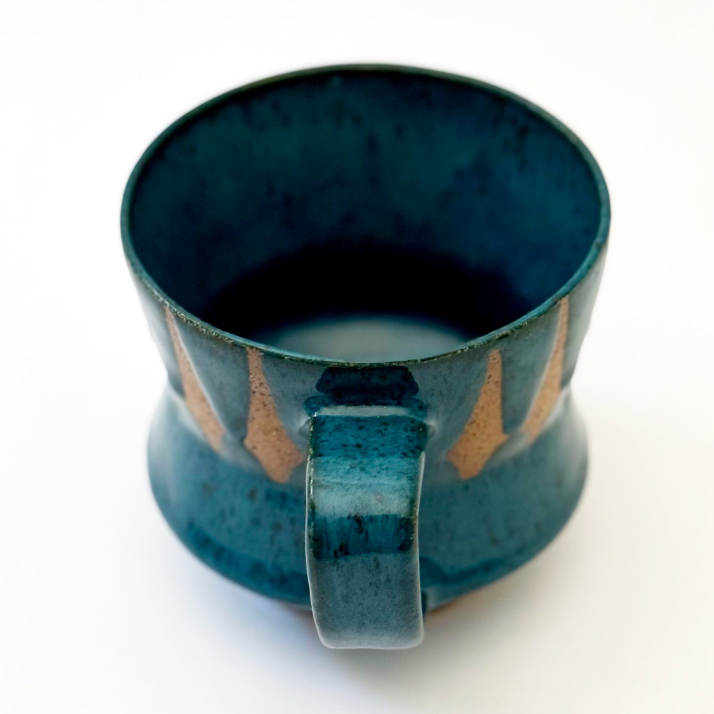 Hand-thrown stoneware mug with layered cobalt and teal blue glaze and a repeating retro geometric pattern in exposed speckled clay. The sculpted mug has a curved waist, angular handle, glossy finish, and mid-century-inspired design. Photographed against a soft white background.