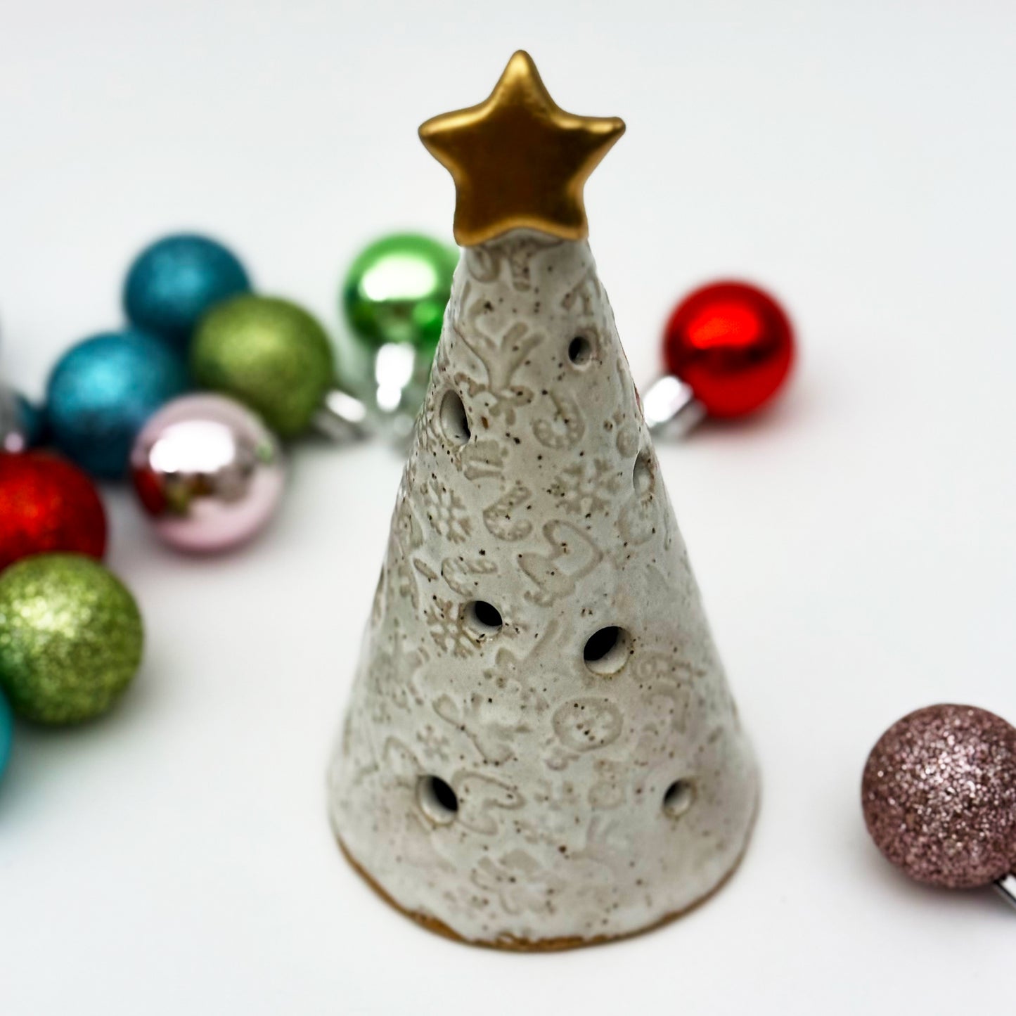 Decorative ceramic christmas tree luminary with a star on top, surrounded by colorful Christmas ornaments.