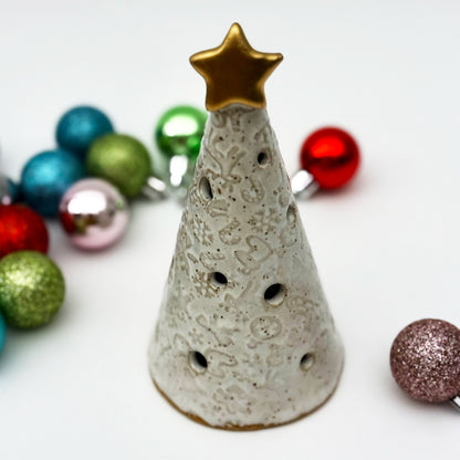 Decorative ceramic christmas tree luminary with a star on top, surrounded by colorful Christmas ornaments.